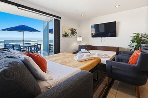 A hotel room with a bed, a desk, a chair, a TV, and a balcony with a view of the ocean. - Ocean Park 09 (San Diego)