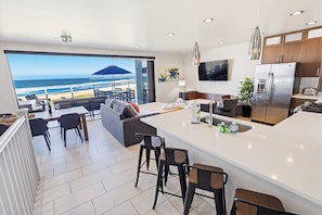 Ett modernt hotellrum med en stor balkong, ett kök med kylskåp och en matplats med utsikt över stranden.