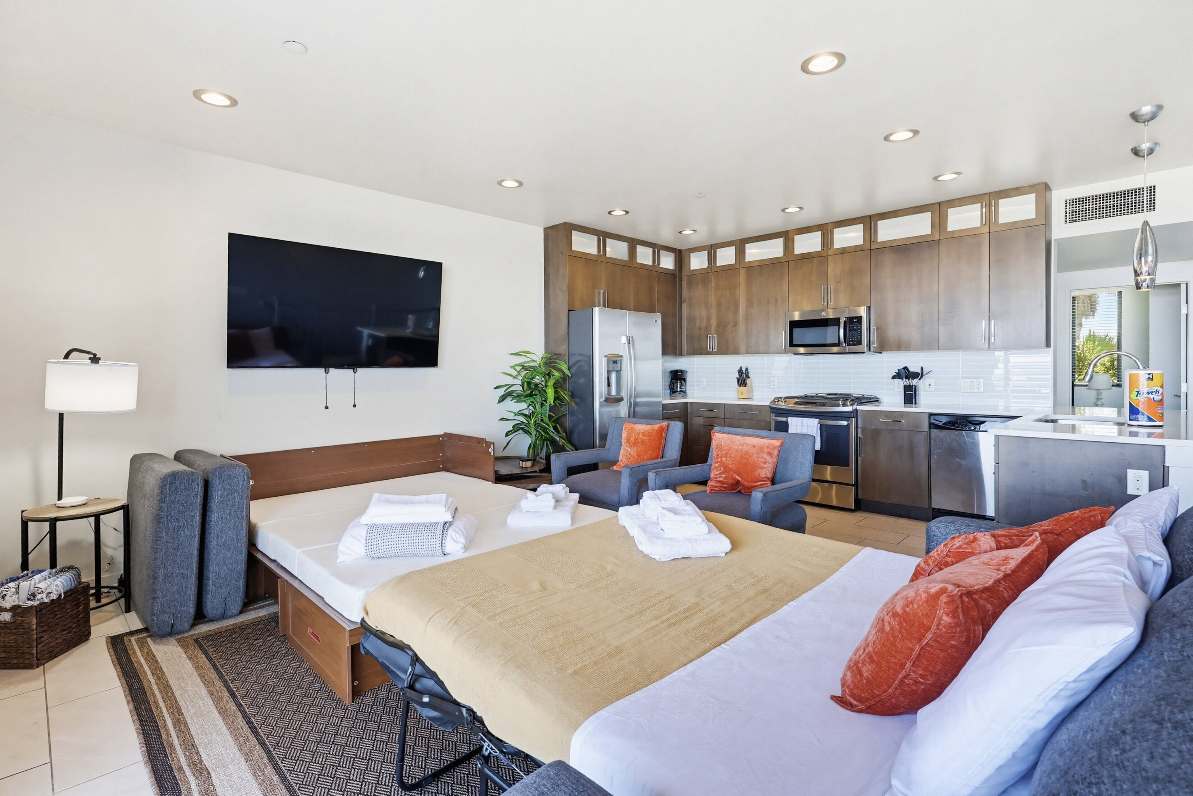 A hotel room with a bed, a TV, a kitchenette, and a seating area.