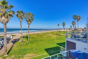 Uitzicht op een strand met palmbomen, een heldere lucht en een modern gebouw met balkon.