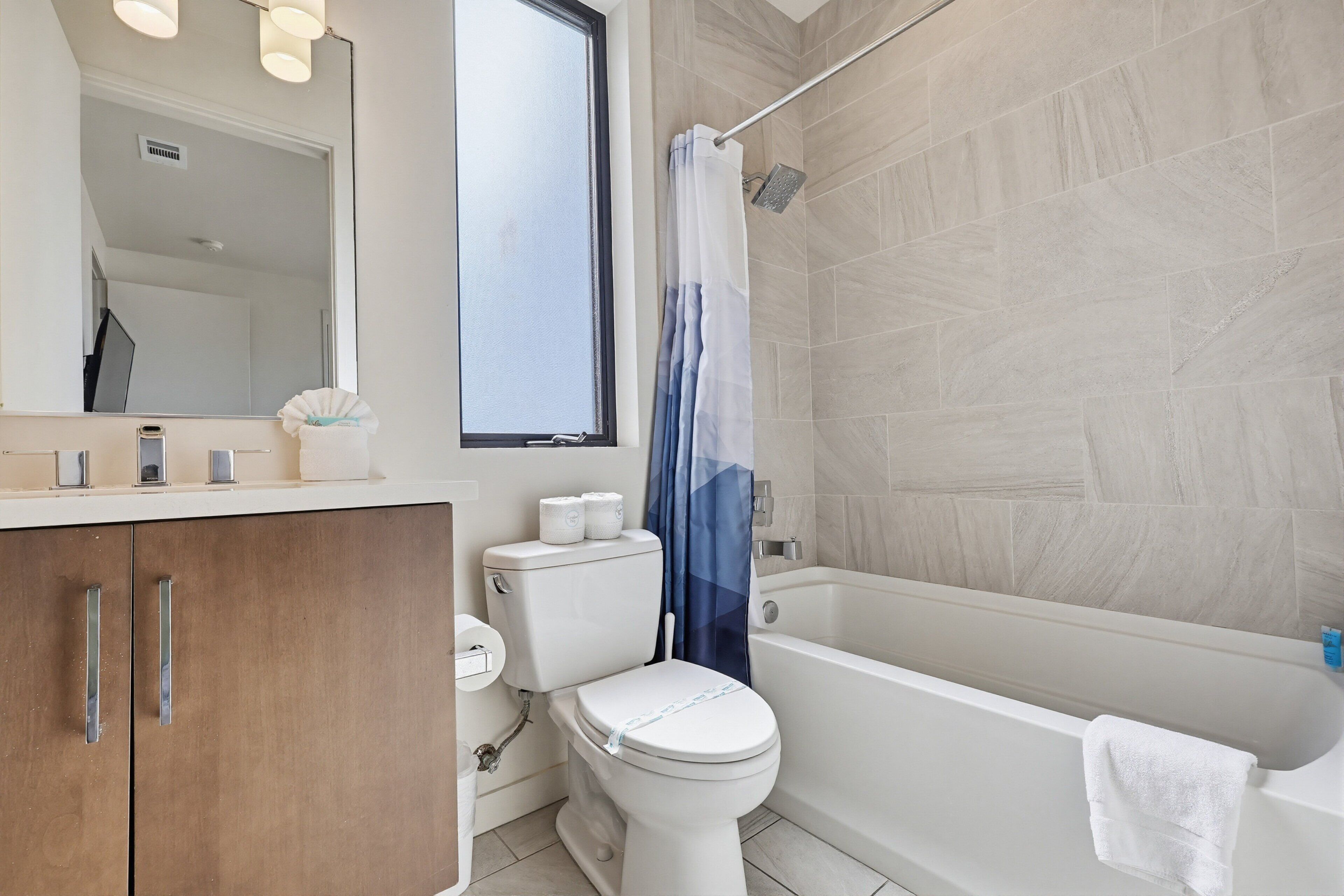 A bathroom with a toilet, a bathtub, a shower curtain, and a mirror.