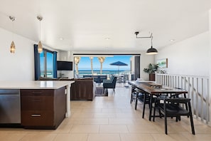 Una cocina moderna con lavavajillas incorporado, una zona de comedor con mesa y sillas de madera, y vista al océano a través de amplios ventanales.