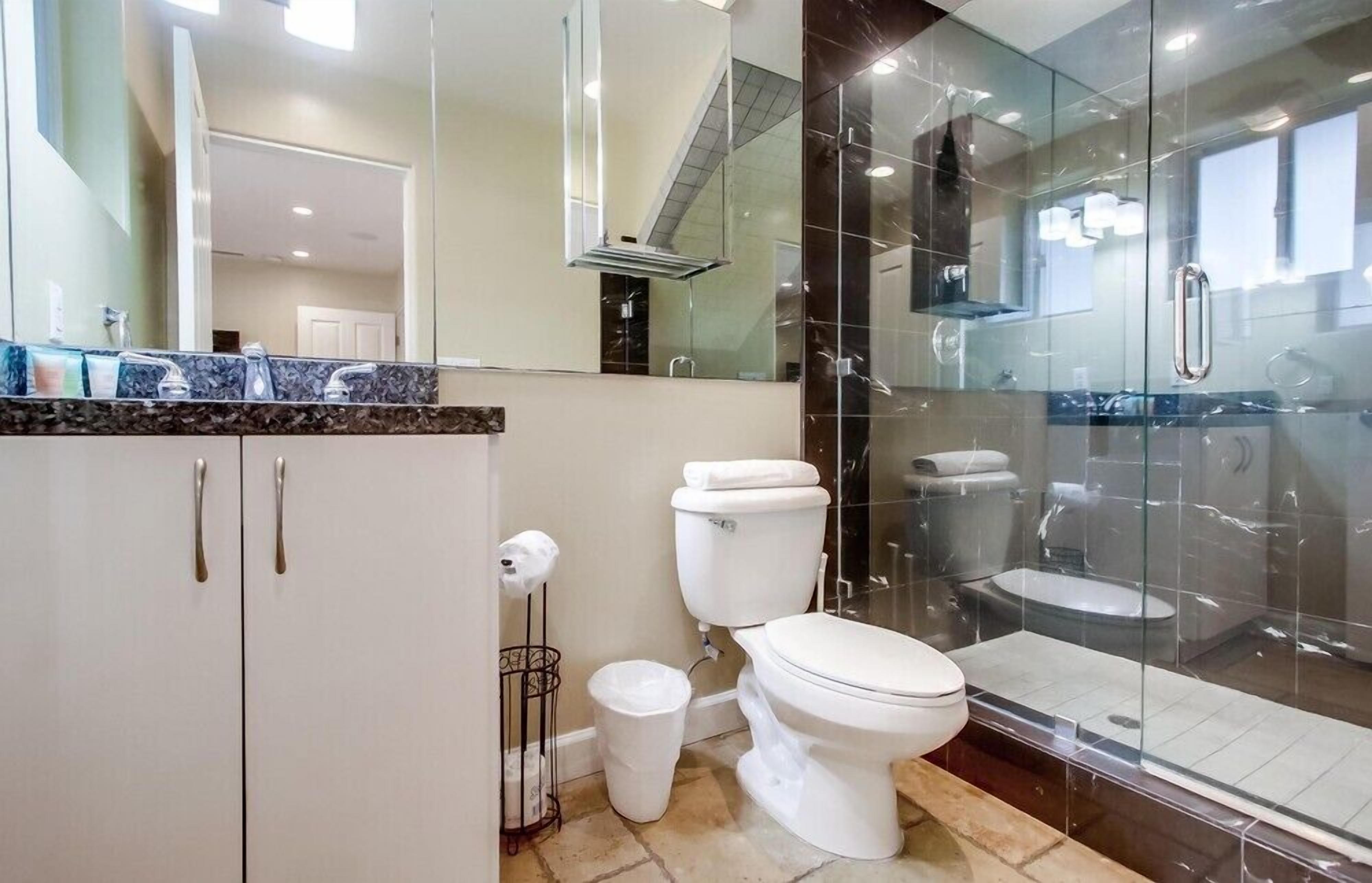 A modern bathroom with a glass shower enclosure, a white toilet, and a marble countertop.
