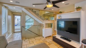A modern living room with a large flat-screen TV, a ceiling fan, and a staircase leading to an upper level. - Ocean View Luxury 2 (San Diego)