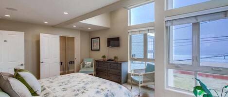 A bedroom with a bed, dresser, TV, and a view of the outside.