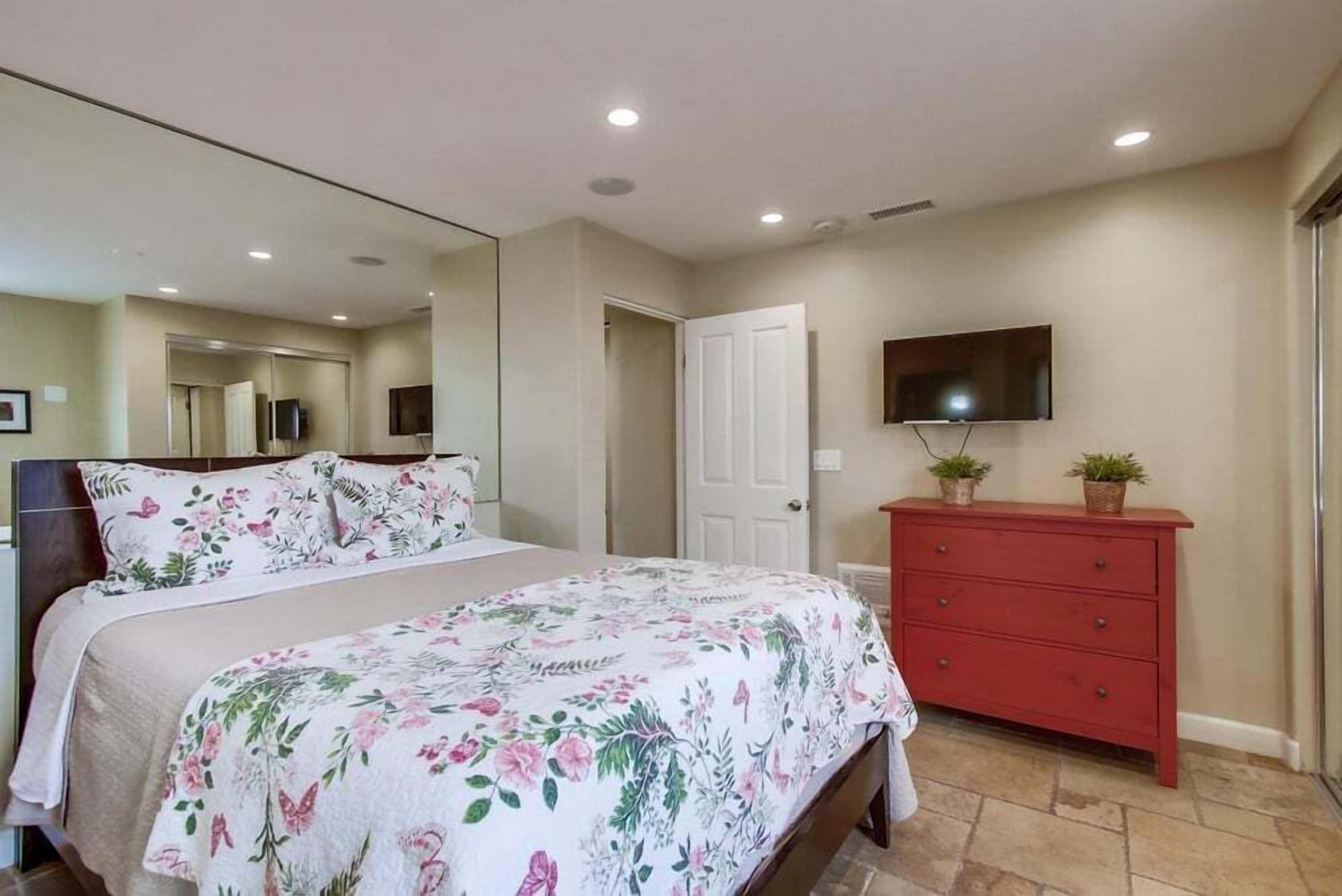 Une chambre à coucher avec un lit, une commode, un téléviseur et une porte.