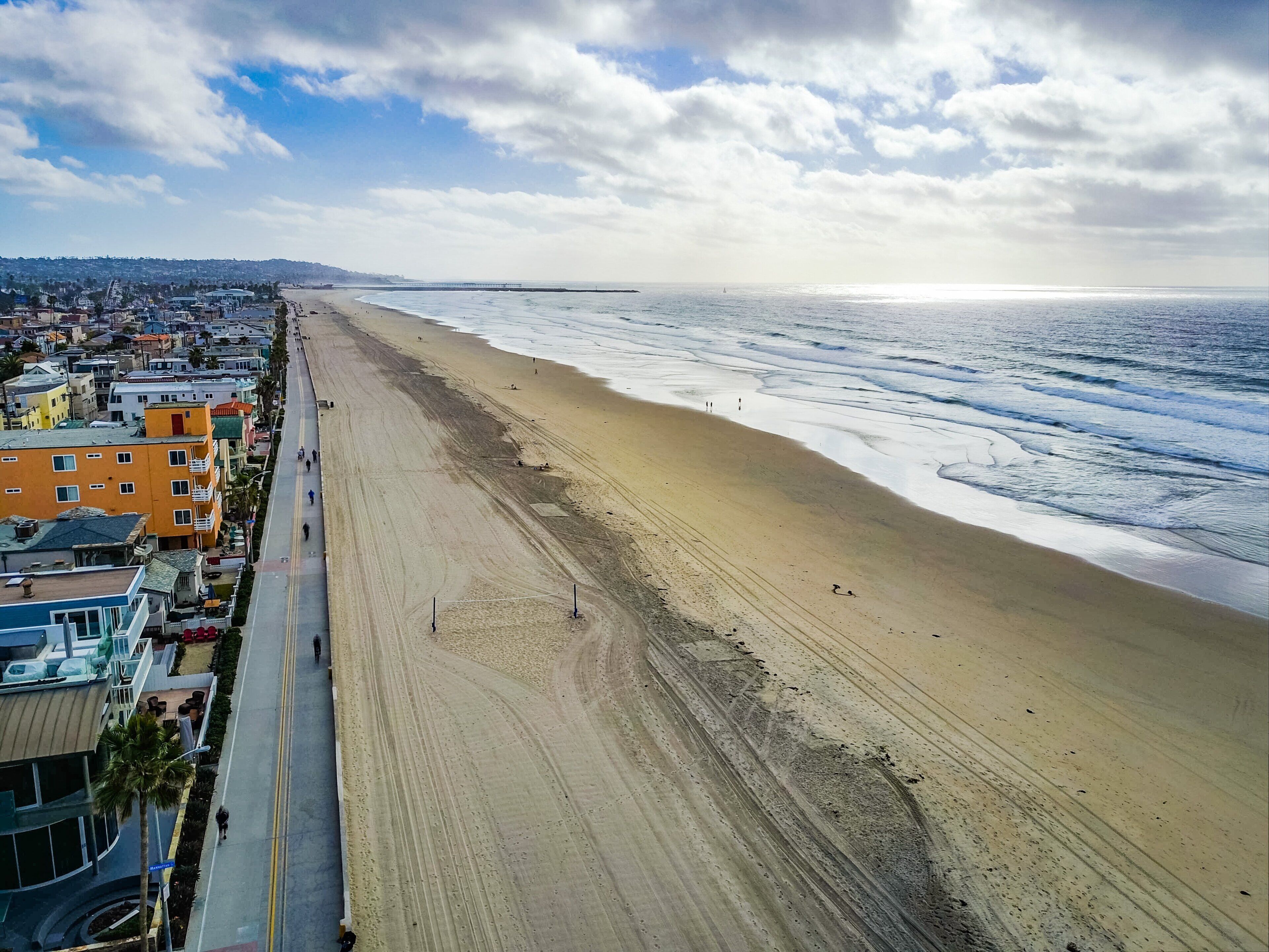 A coastal cityscape with a wide beach, a long road parallel to the shore, and buildings lining the beachfront.