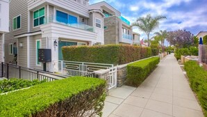 A modern multi-story residential building with a gated entrance, a well-maintained pathway, and a clear view of the surrounding greenery. - Pacific Pearl (San Diego)