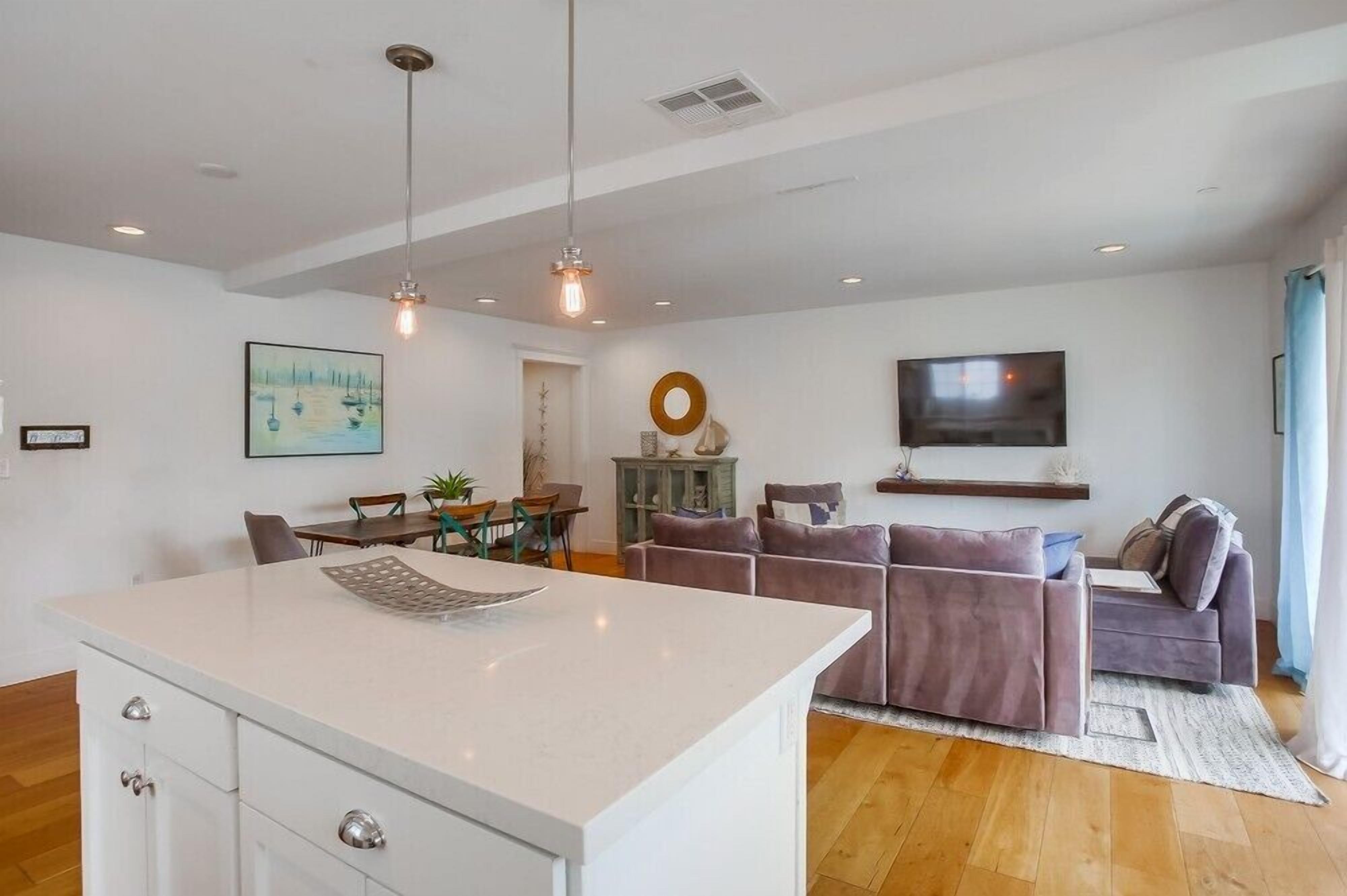 A modern living room with a sofa, a dining table, and a TV mounted on the wall.