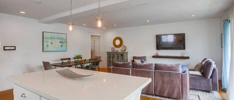 A modern living room with a sofa, a dining table, and a TV mounted on the wall.