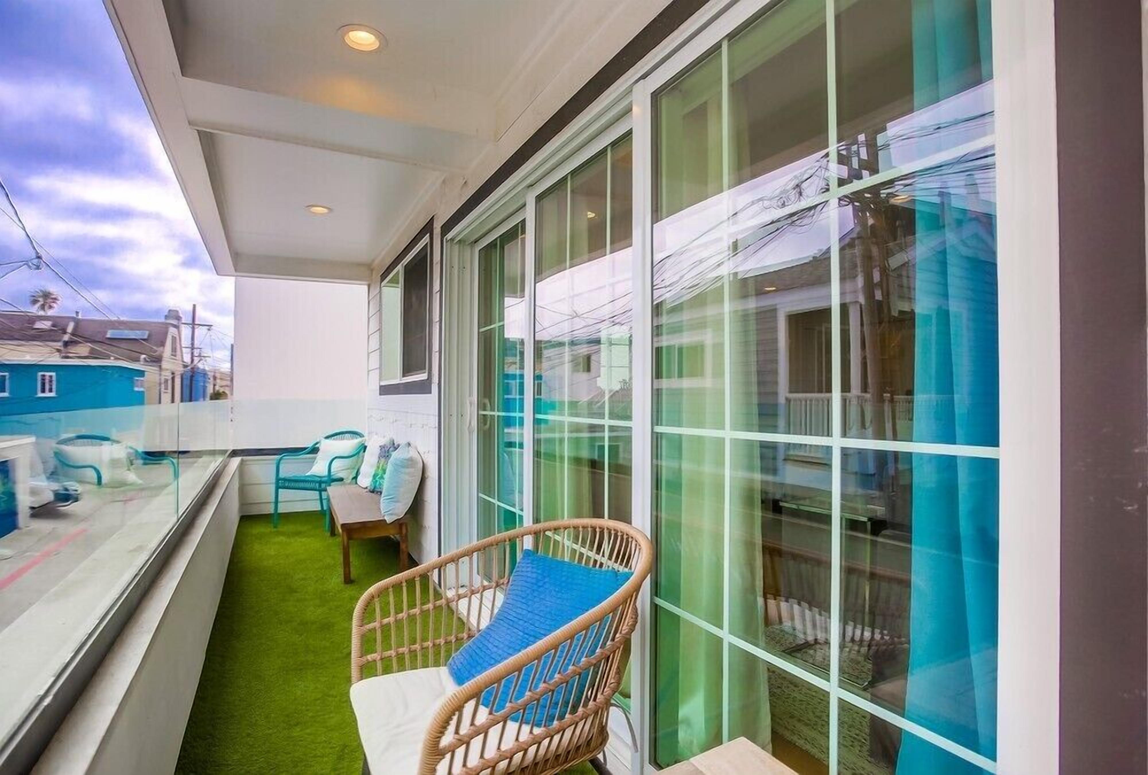 A balcony with a green artificial turf, wicker chairs, and a table.