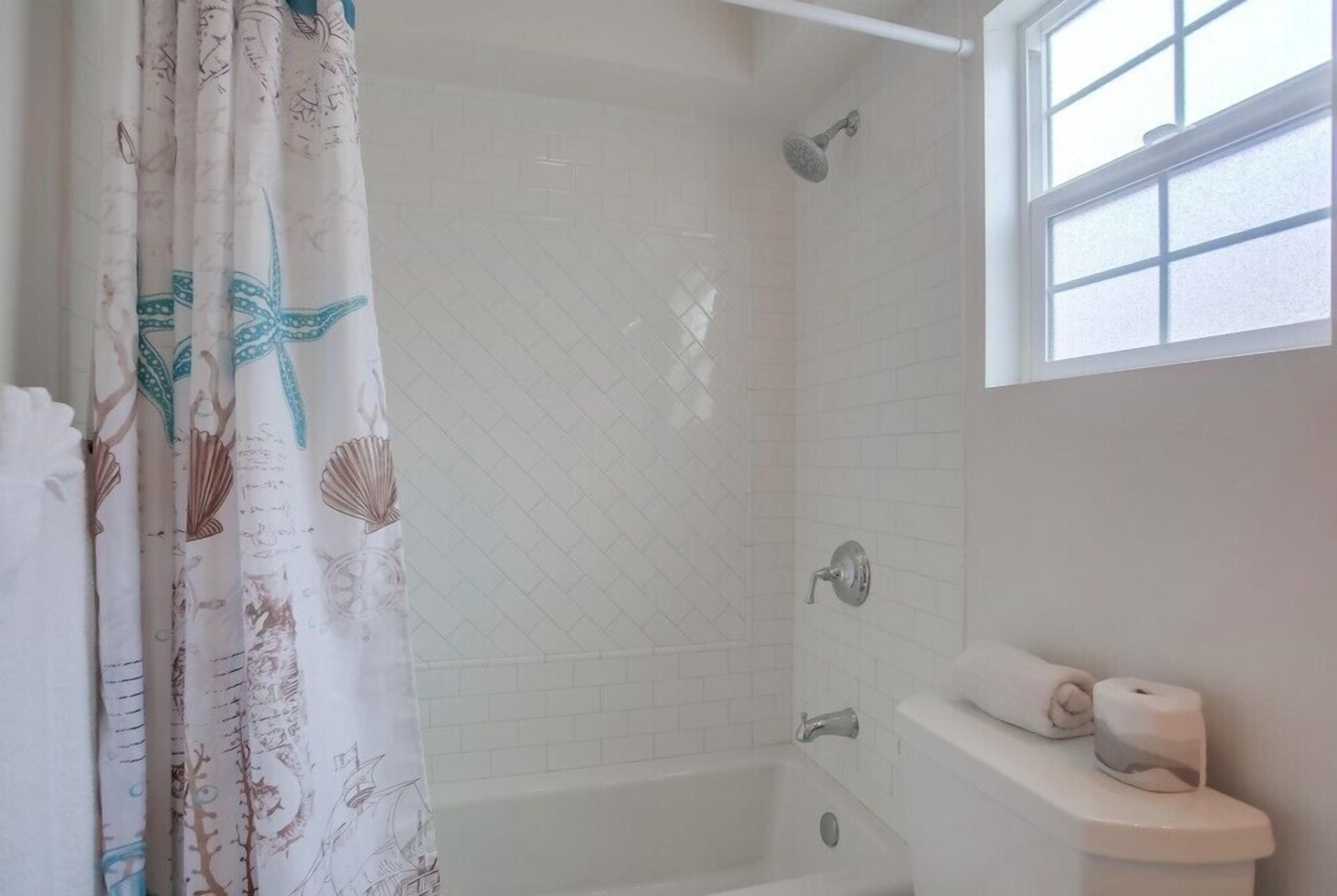 A bathroom with a shower, a toilet, and a window.