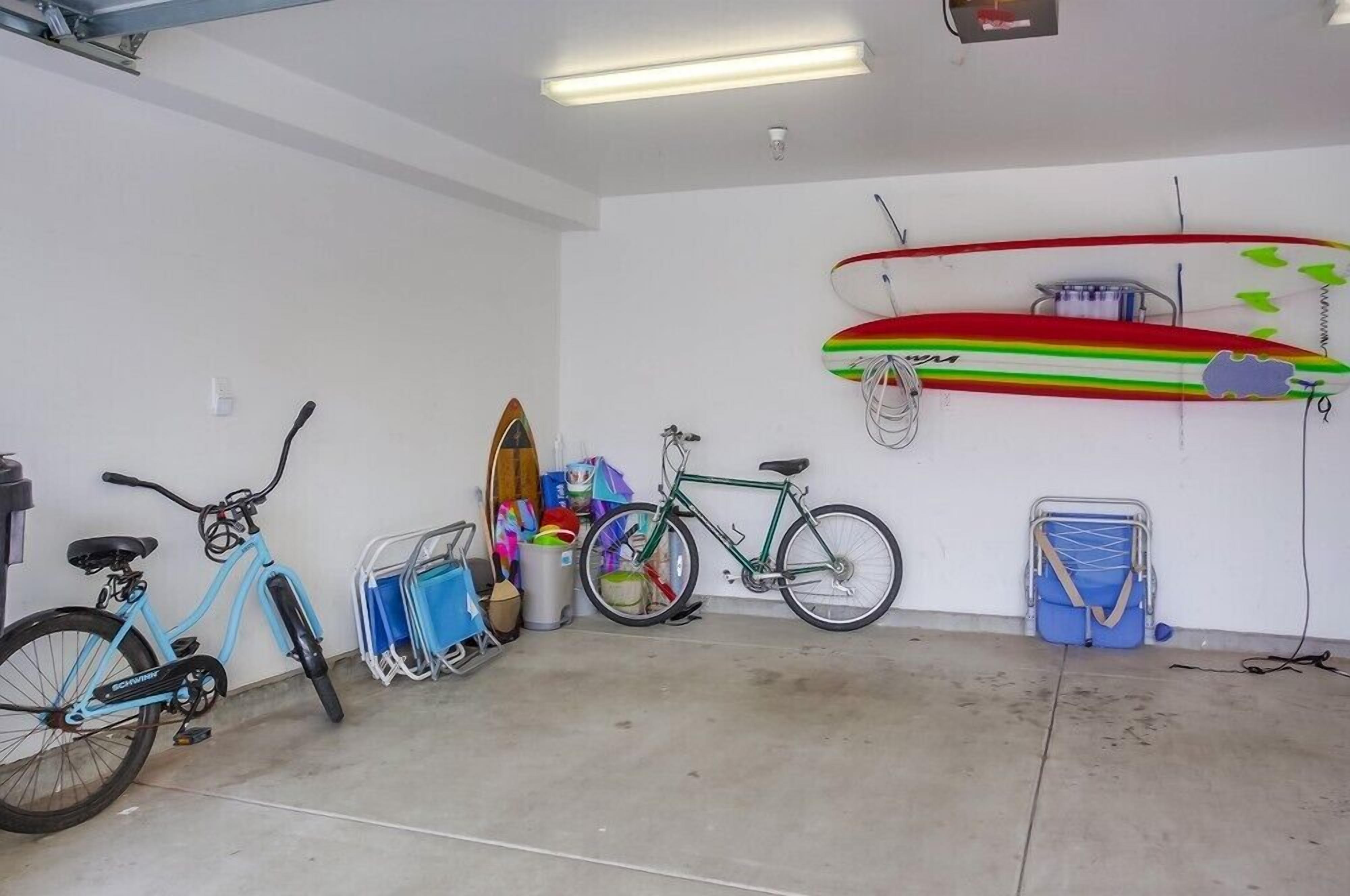 Un garaje con bicicletas, una tabla de surf y contenedores de almacenamiento.
