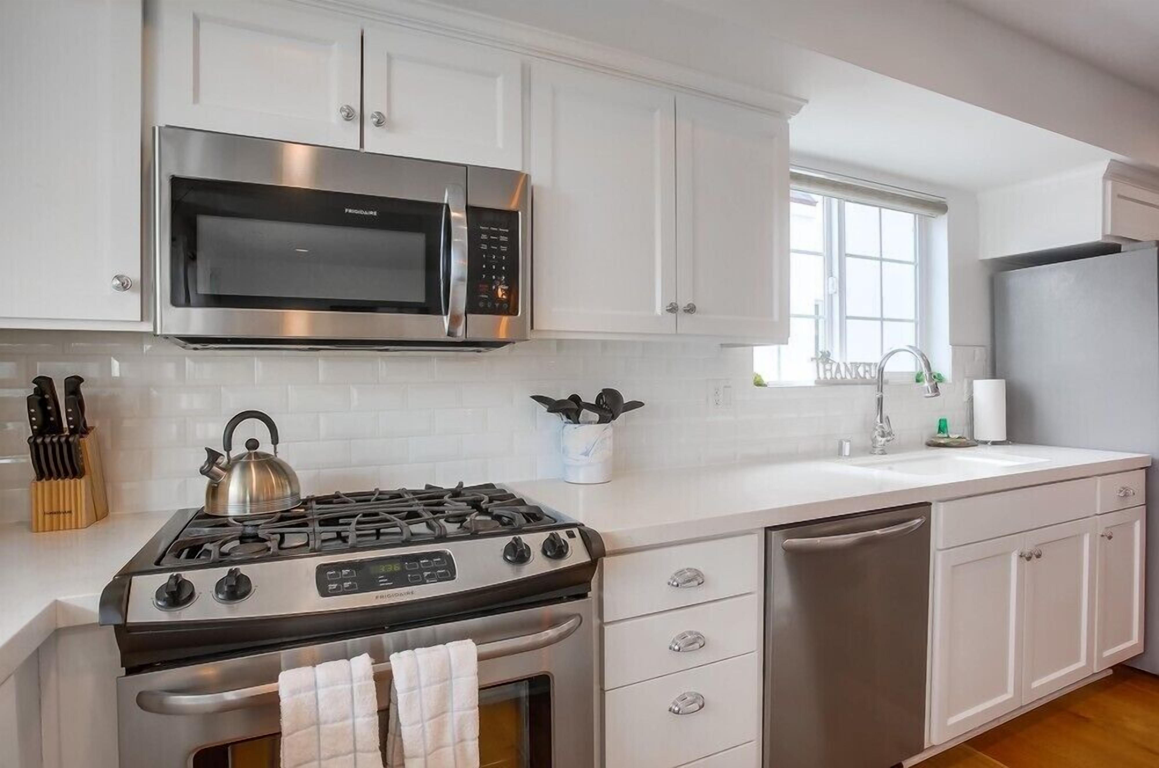A modern kitchen with white cabinetry, a stainless steel stove, a microwave, and a dishwasher.