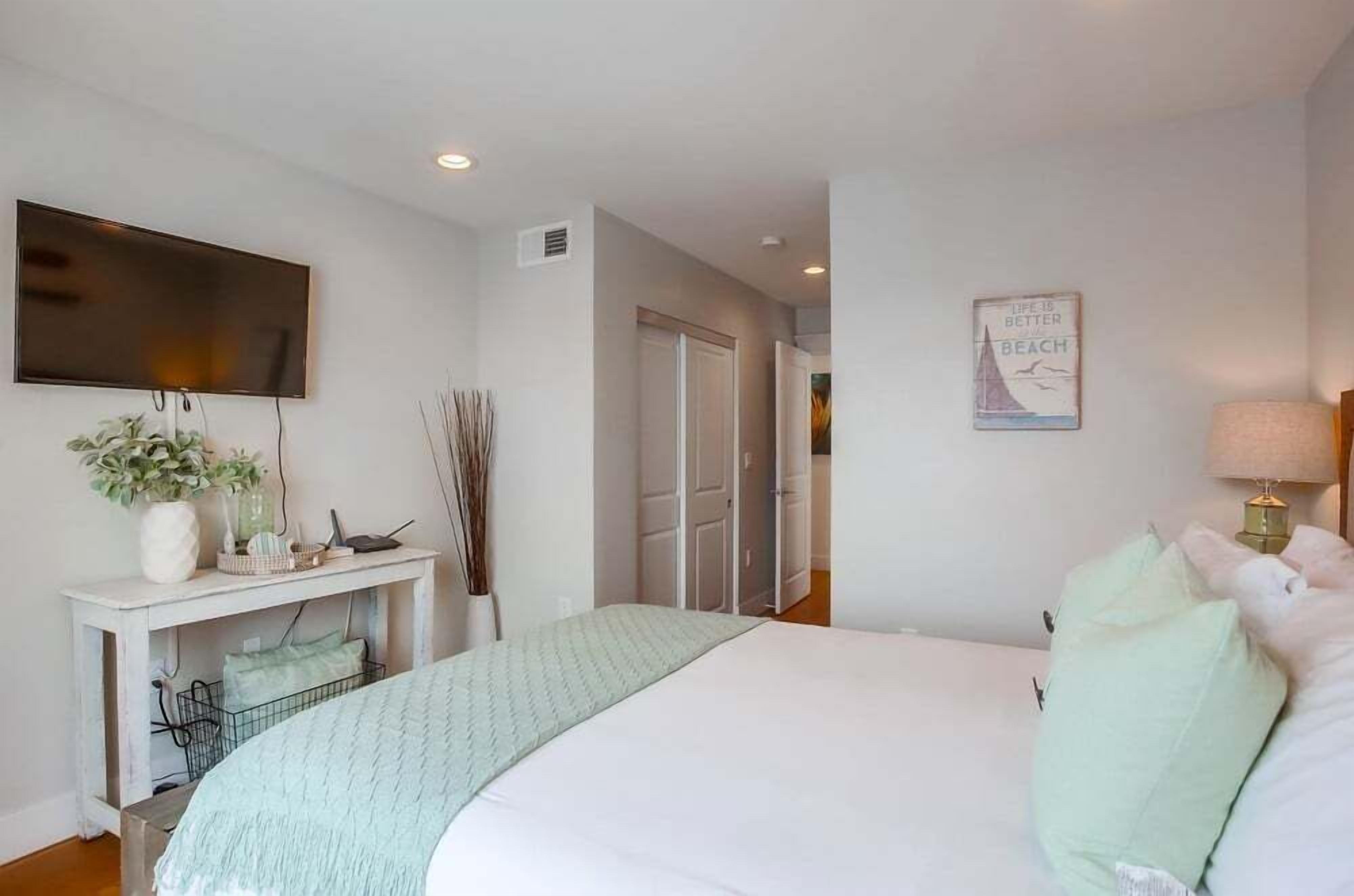A bedroom with a bed, a desk, a television, and a wall-mounted lamp.