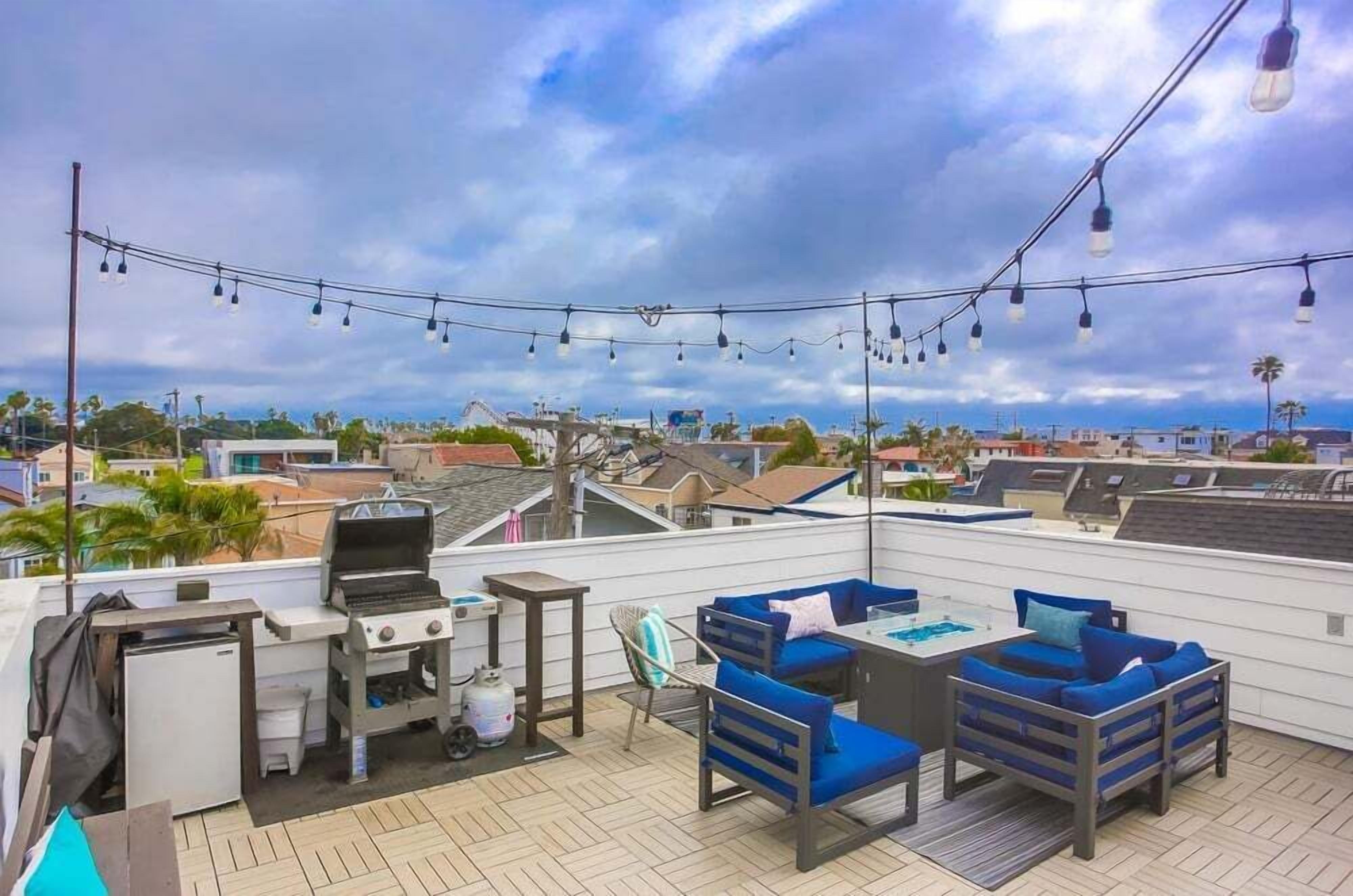 A rooftop patio with a grill, seating area, and string lights.