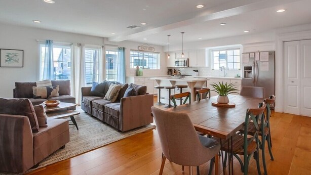A spacious living room with a large dining table, sofas, and a kitchen area with a refrigerator and cabinets. - Pacific Pearl (San Diego)