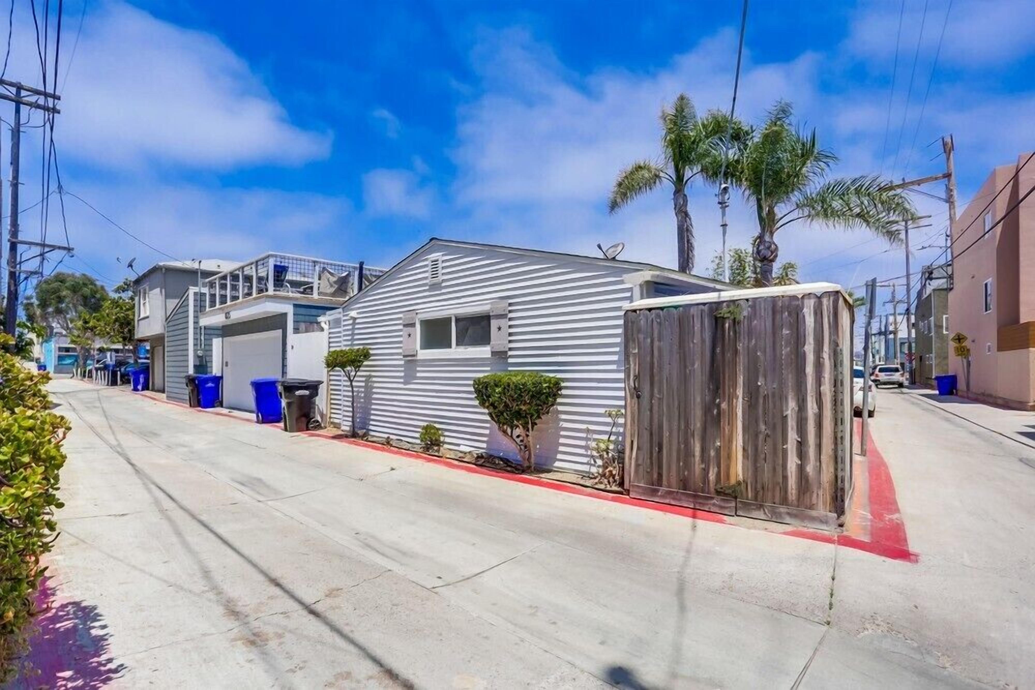 A residential street with a single-story house, a wooden fence, and a red curb.