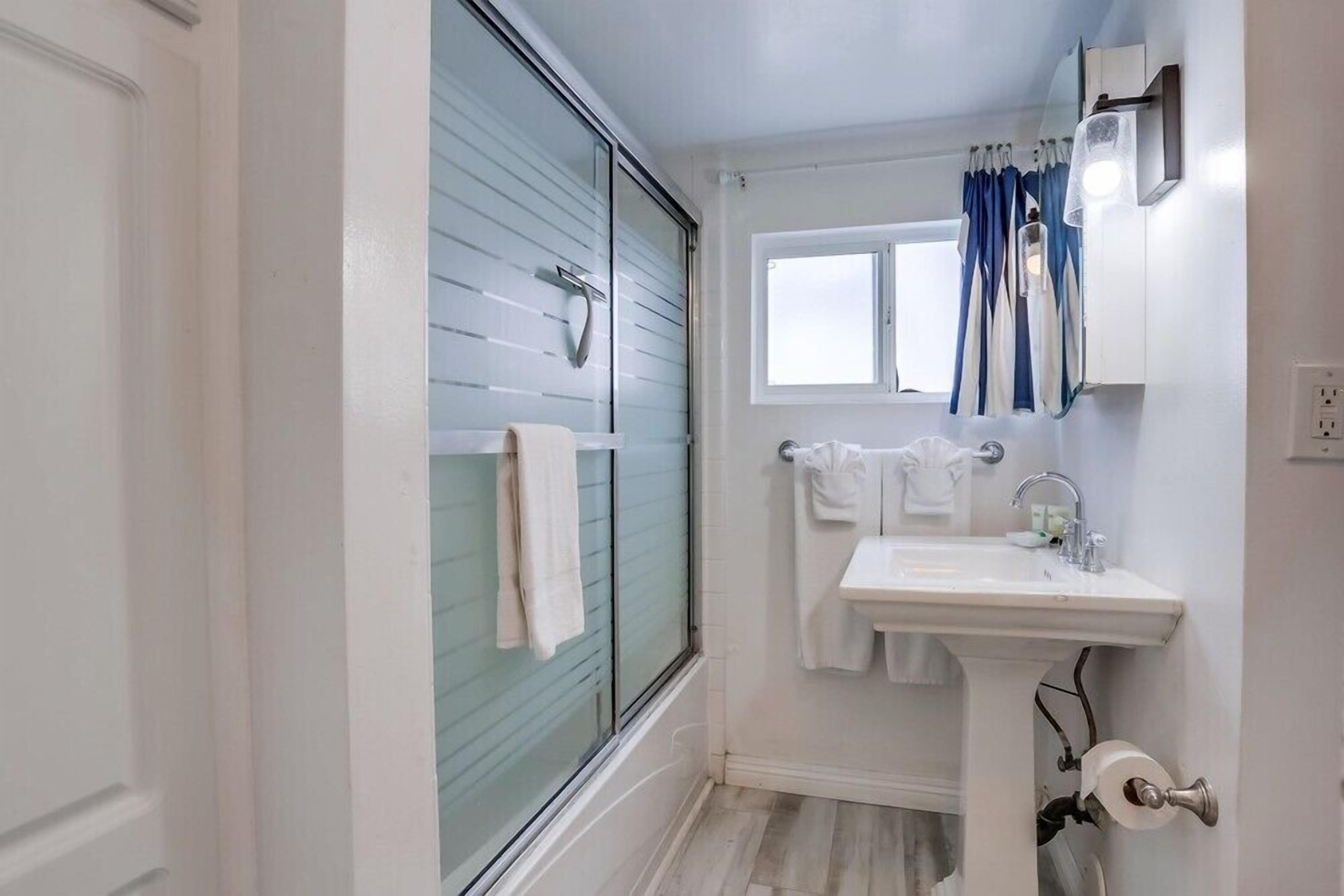 A bathroom with a glass shower door, a sink, and a window.
