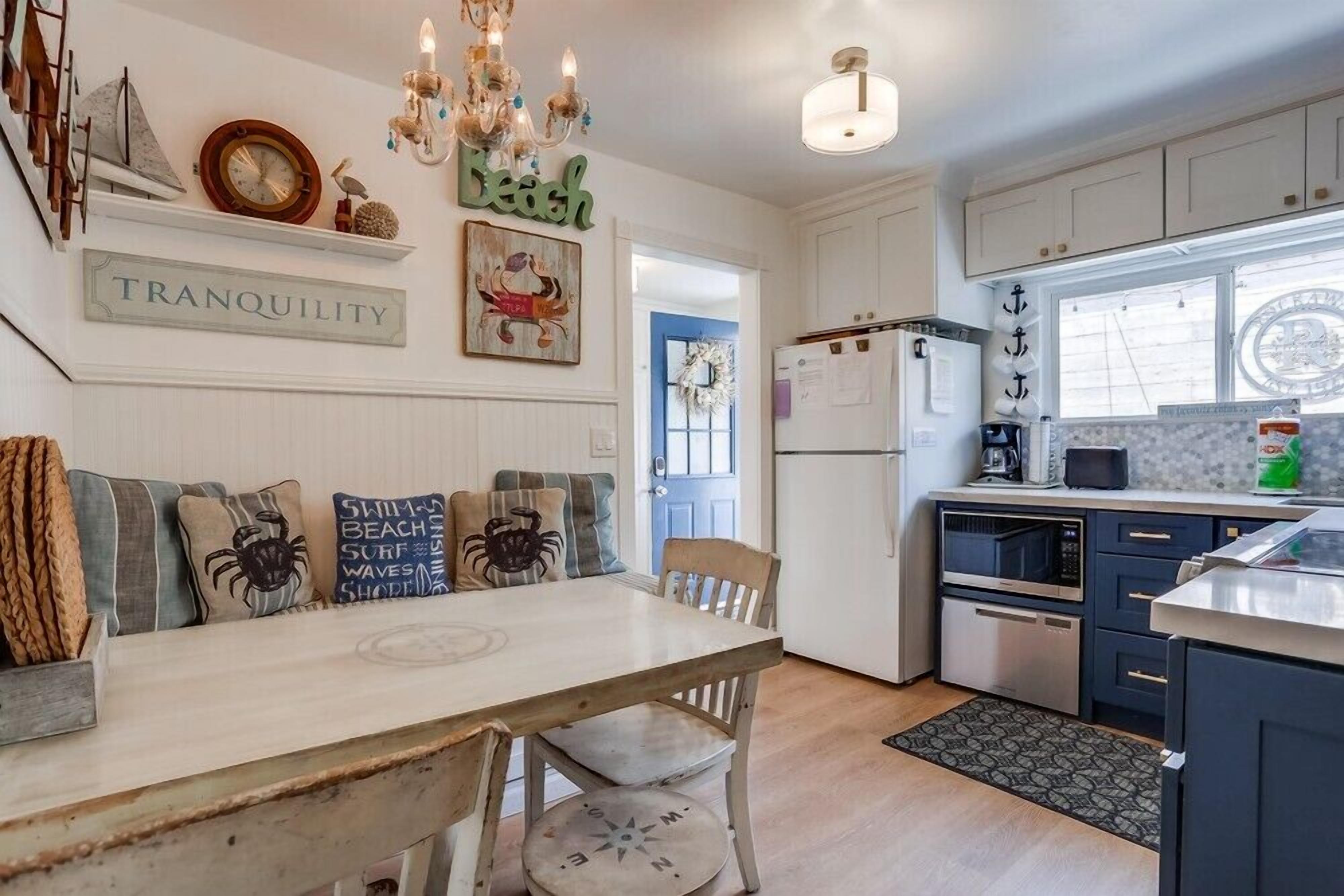 A kitchen with white cabinets, a dining table with nautical-themed cushions, and a chandelier.