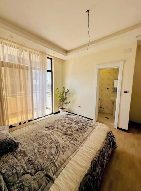 Relax in this serene bedroom with a large bed and a potted plant on the windowsill.