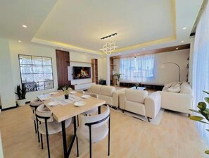 Relax in this inviting living room with a large TV, comfortable seating, and a dining table for four.