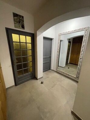 Un corridoio con una porta che presenta un pannello in vetro satinato, un grande specchio decorativo e un pavimento piastrellato.