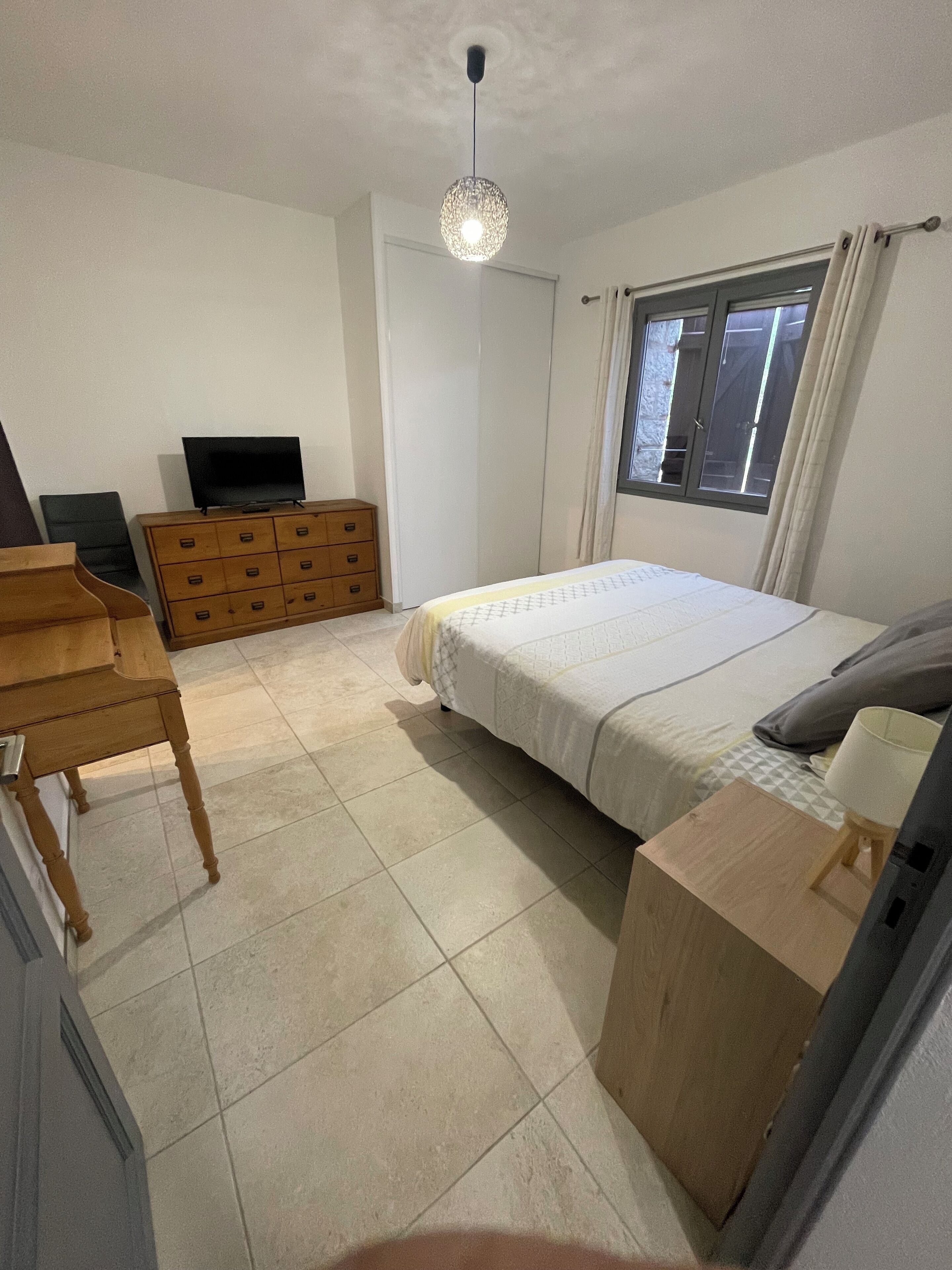 Un dormitorio con una cama, un aparador de madera, un televisor y una ventana con cortinas.