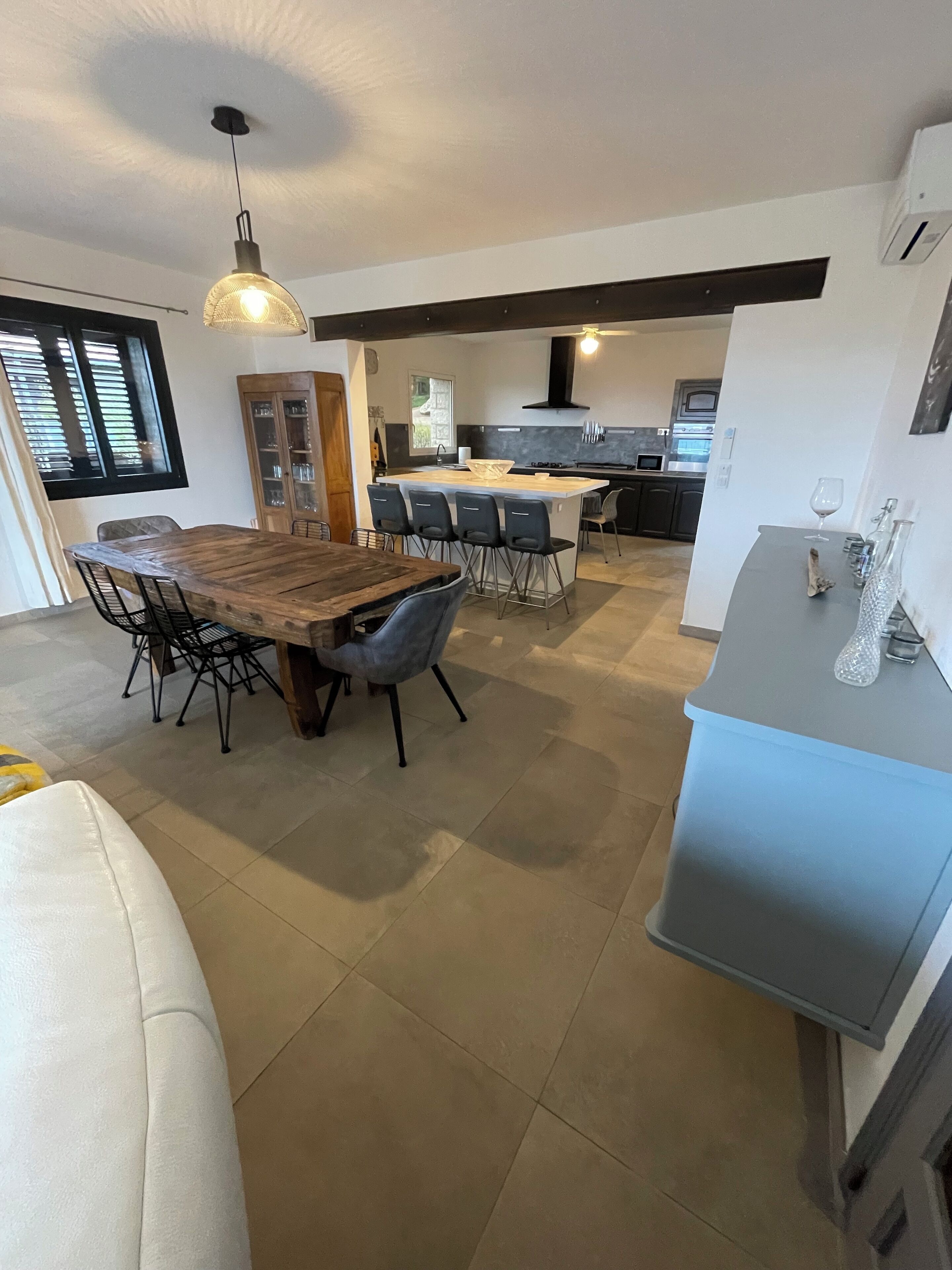 Una cocina moderna con una isla central, taburetes de bar y una zona de comedor con una mesa y sillas de madera.