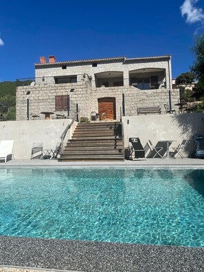 Un edificio in pietra a due piani con una piscina di fronte.