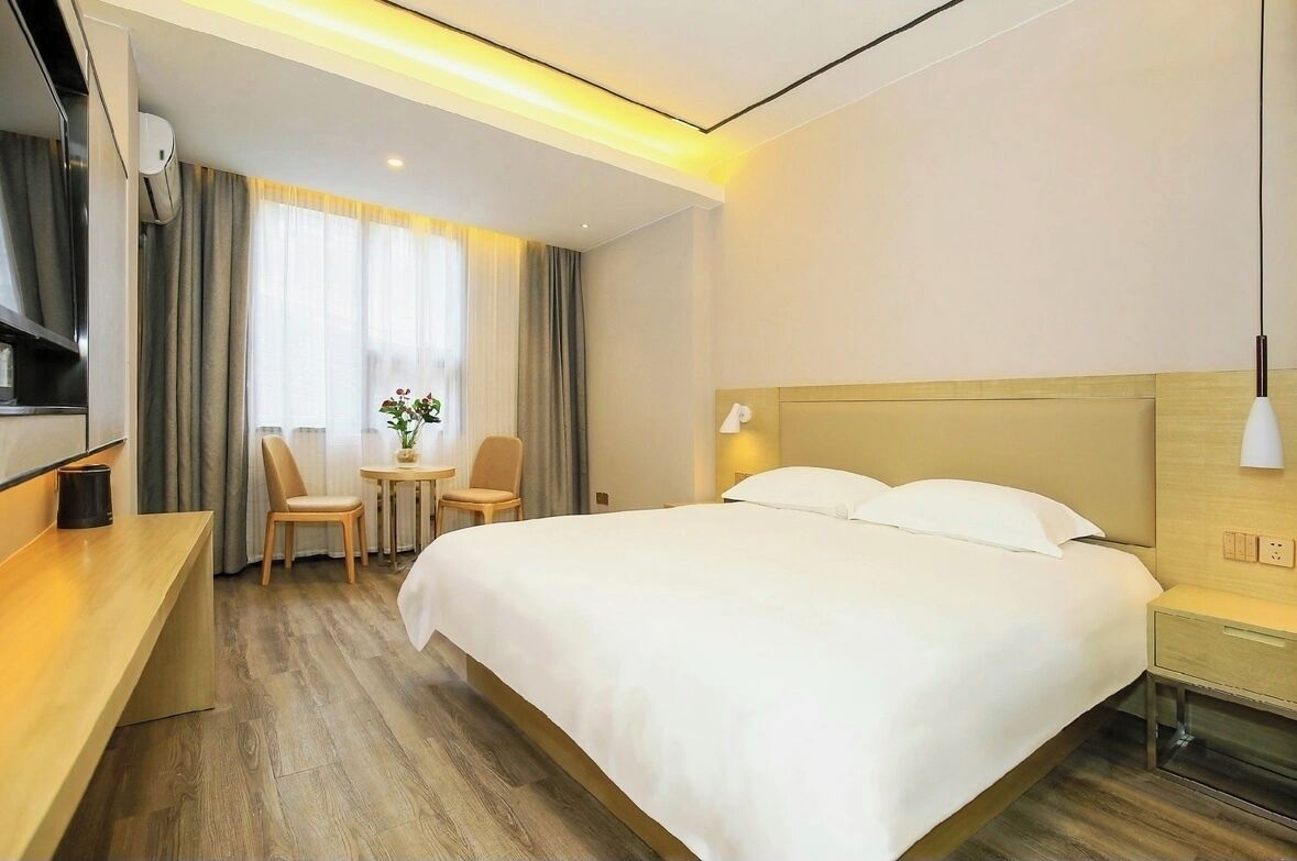 Una habitación de hotel con una cama grande, un escritorio, una silla, una mesita con una planta y una ventana con cortinas.