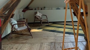 A rustic attic room with exposed wooden beams, a slanted ceiling, and a skylight. There are two wicker chairs and a small table with a lamp. - Cocoon House – Private Garden & Exposed Beams – Peaceful Retreat 1h from Paris (Villeblevin)