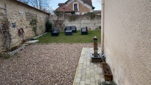A courtyard with a stone wall, a small garden area with a fountain, and a building with a tiled roof in the background. - Cocoon House – Private Garden & Exposed Beams – Peaceful Retreat 1h from Paris (Villeblevin)