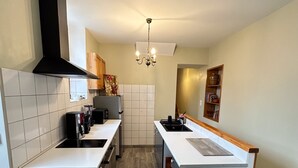 A modern kitchen with white cabinetry, a black range hood, a central island with a sink, and a chandelier. - Cocoon House – Private Garden & Exposed Beams – Peaceful Retreat 1h from Paris (Villeblevin)