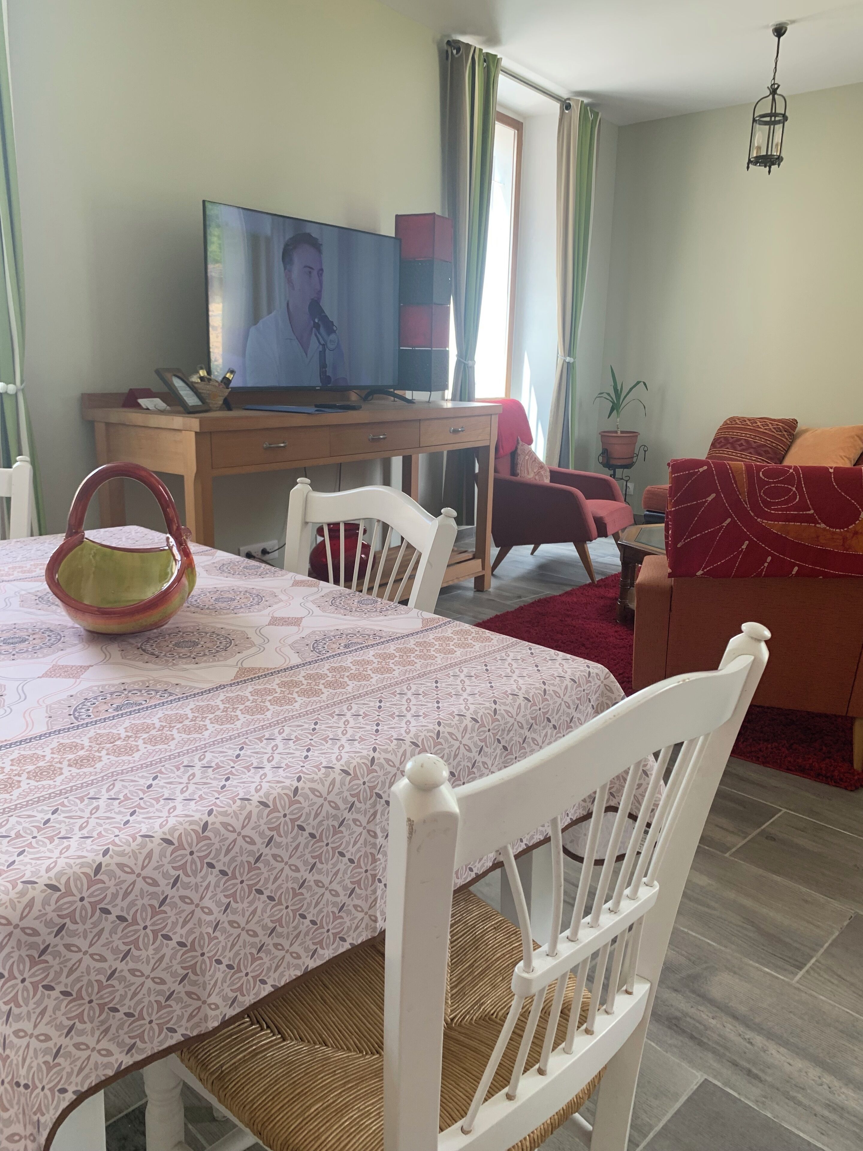 A dining area with a table set for two, a television on a wooden desk, and a red sofa in the background.