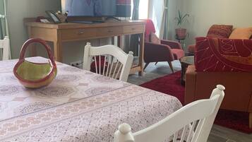 A dining area with a table set for two, a television on a wooden desk, and a red sofa in the background.