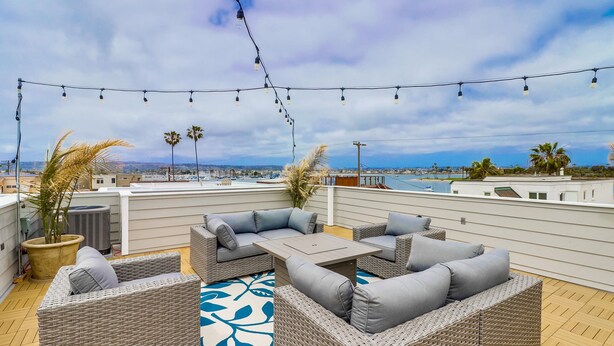 A rooftop patio with wicker furniture, string lights, and a view of the city. - Seaglass Shores (San Diego)