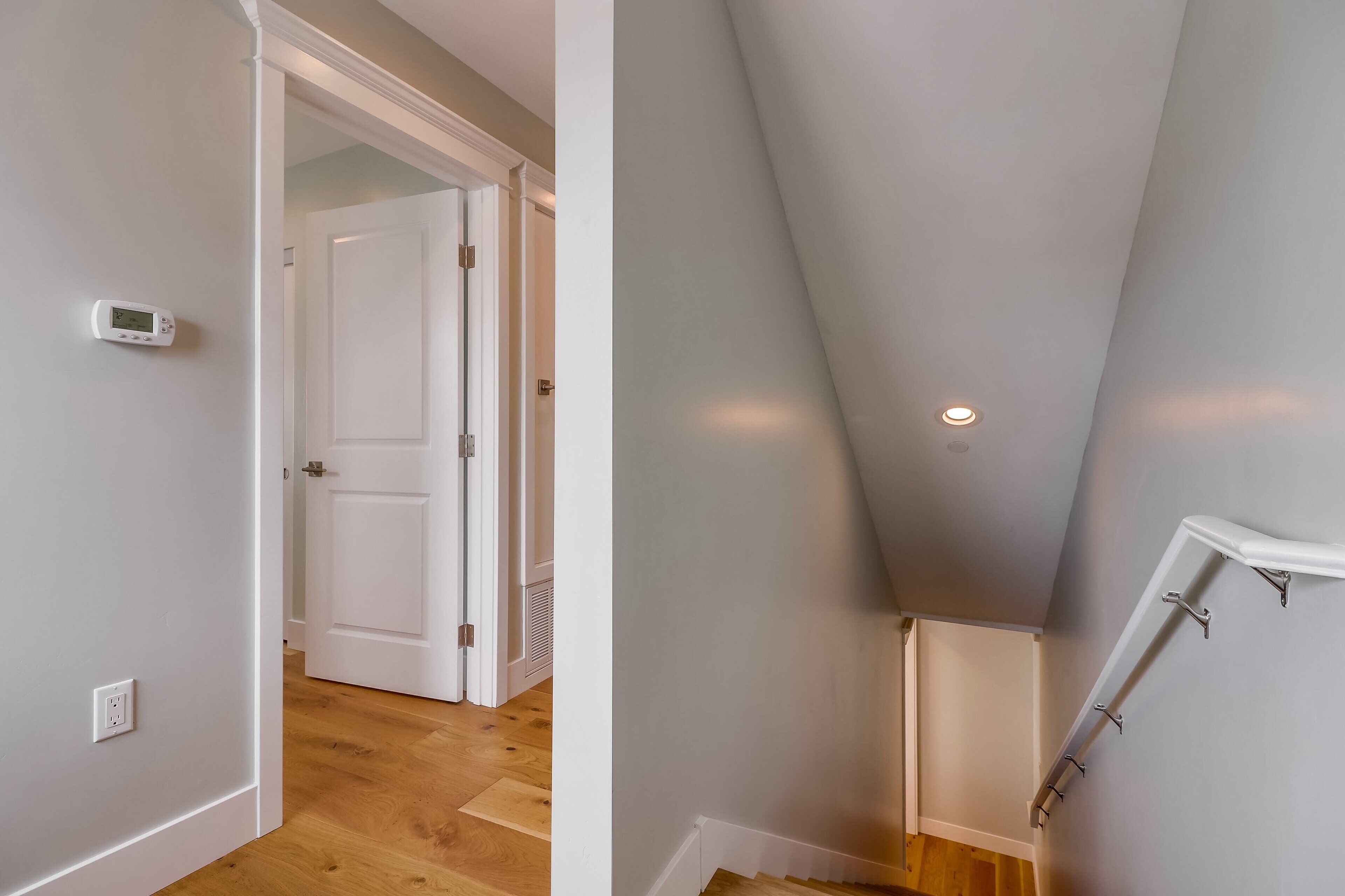 Un interno moderno con pavimento in legno, una porta bianca e una scala con corrimano bianco.