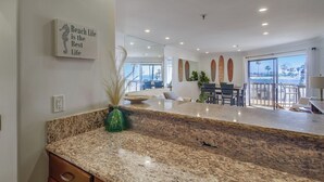A modern kitchen with granite countertops, a decorative seahorse sign, and a view of the dining area. - See the Sea 52 (San Diego)