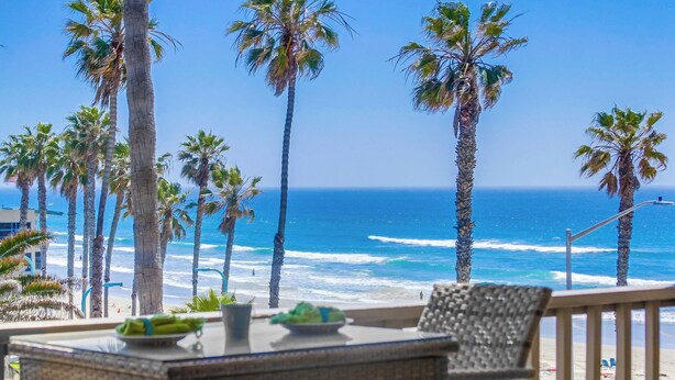 A balcony with wicker furniture overlooking a beach with palm trees and the ocean. - See the Sea 52 (San Diego)