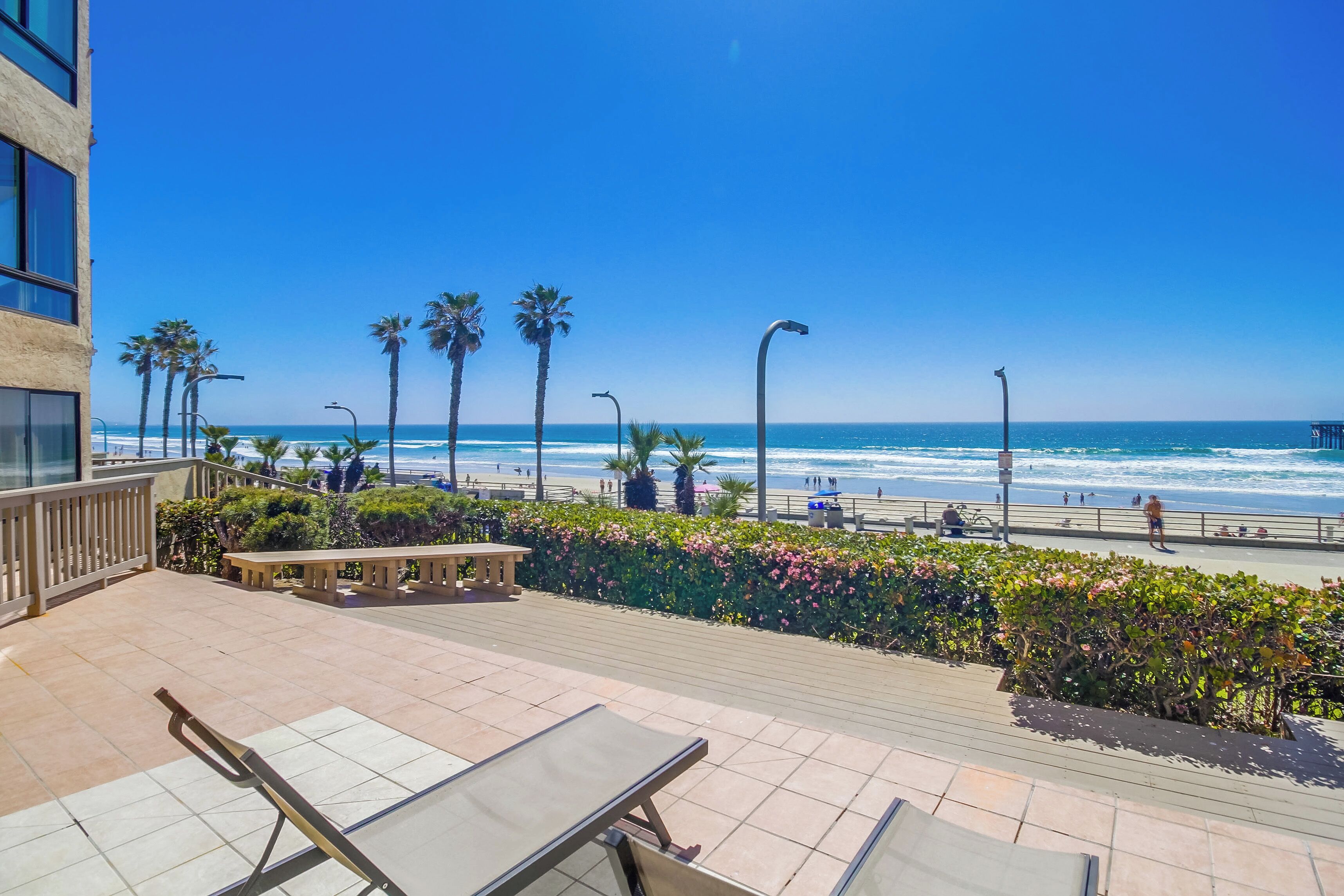 A balcony with a view of the beach, palm trees, and a clear blue sky.