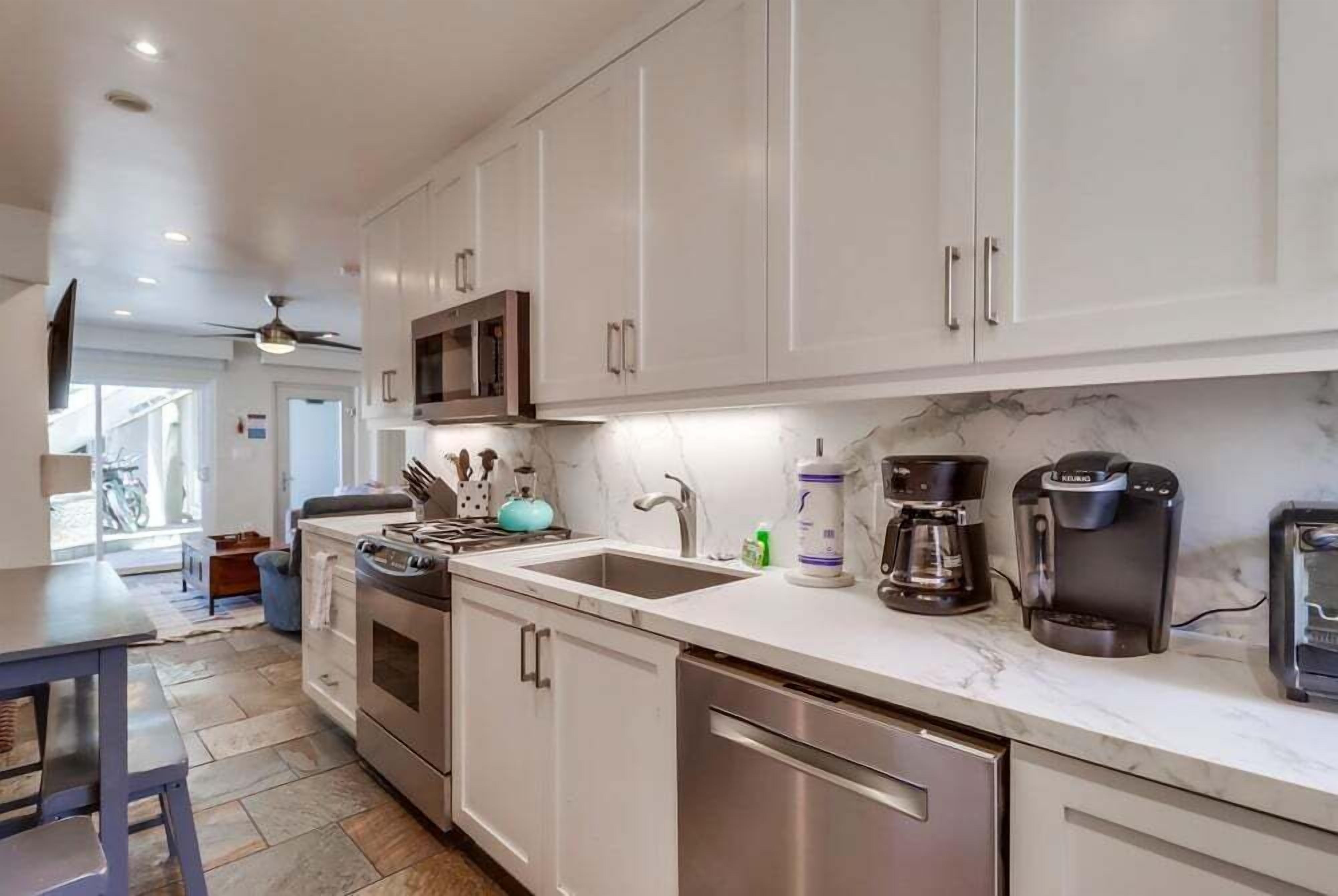 A modern kitchen with white cabinets, stainless steel appliances, a marble countertop, and a ceiling fan.