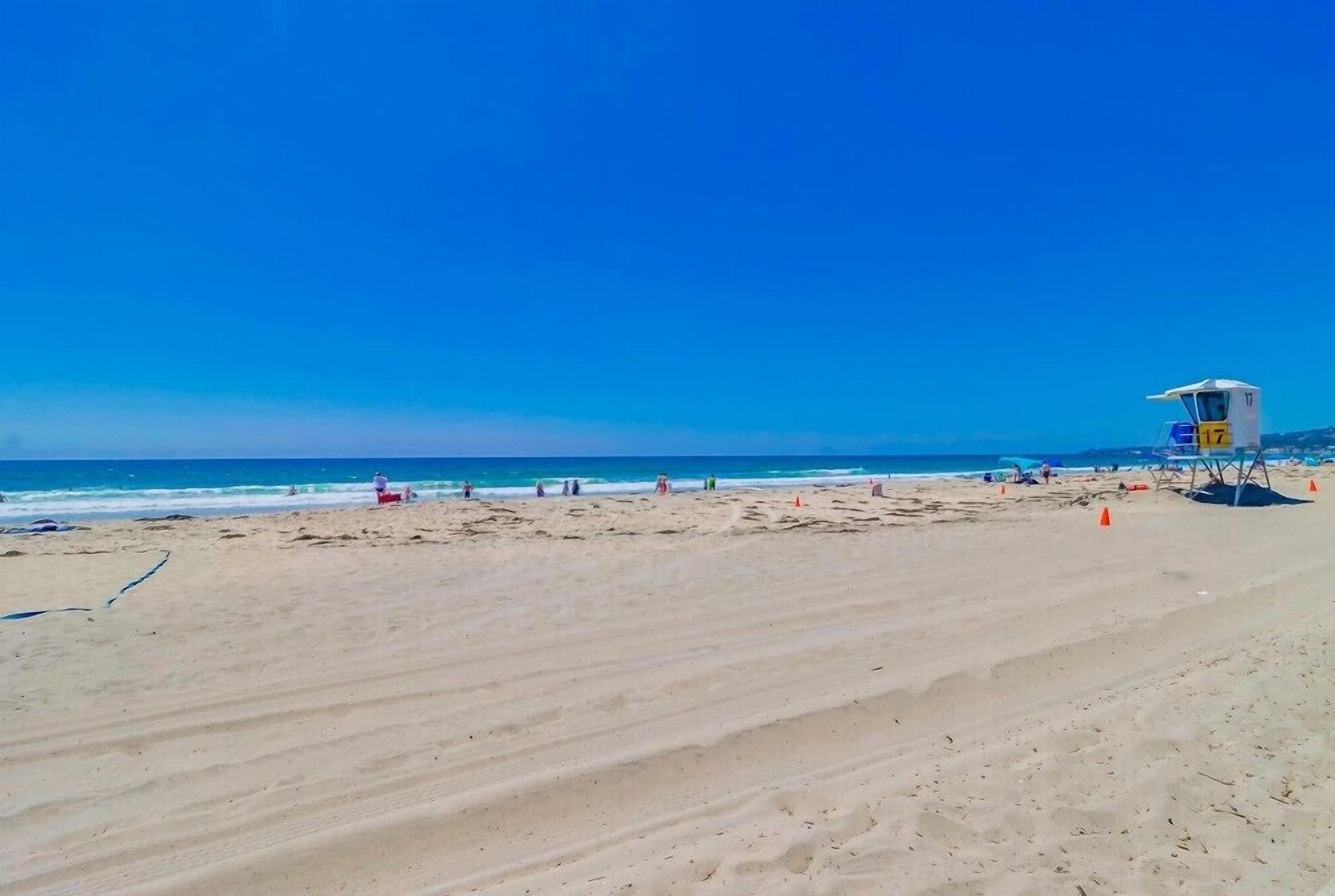 A wide sandy beach with a lifeguard tower and orange cones.