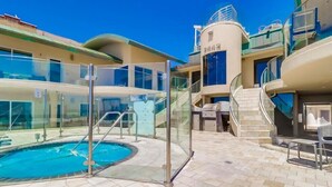 An outdoor swimming pool with glass railings, a staircase, and a building with a beige facade. - Surf Rider D (San Diego)