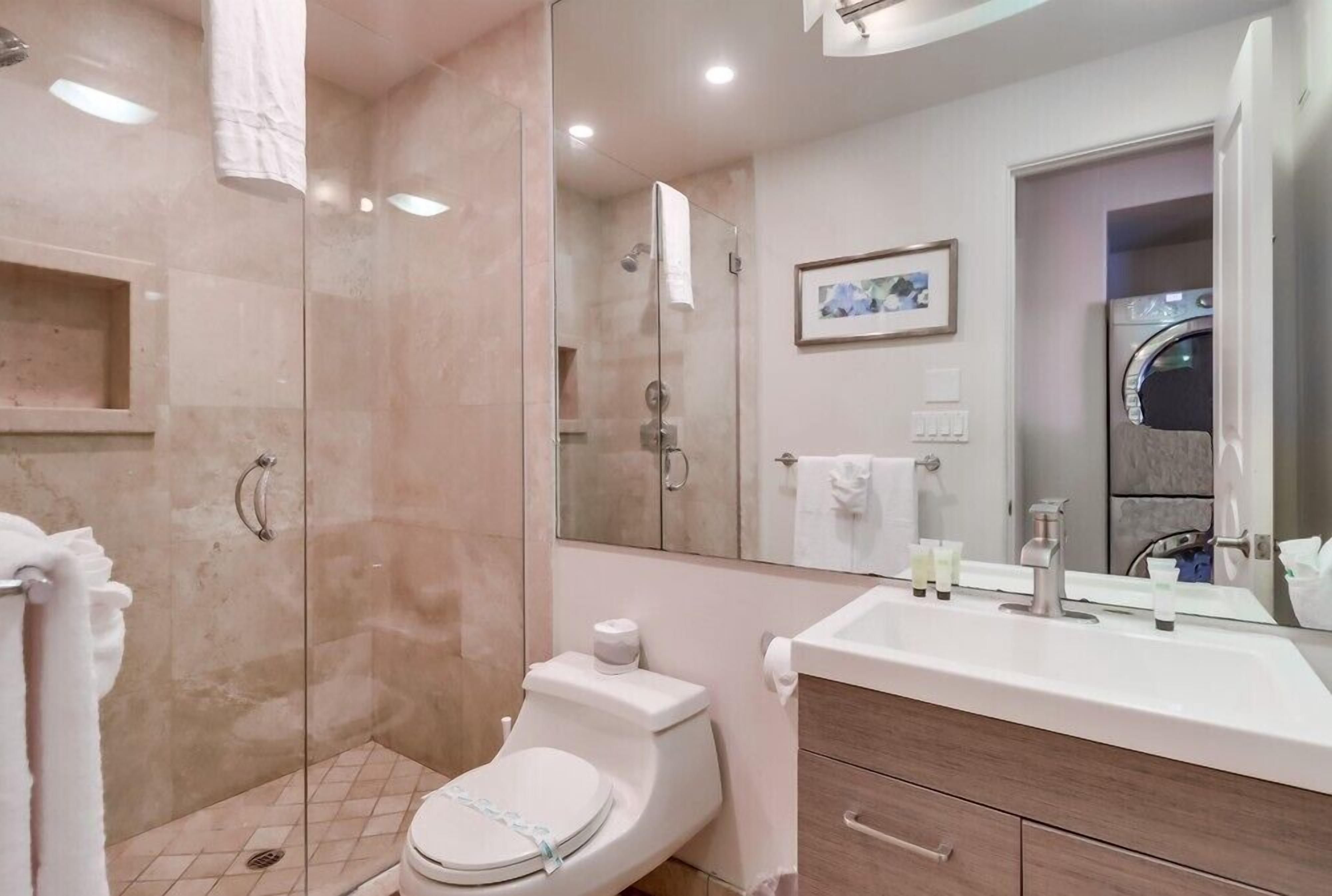 Une salle de bain moderne avec une douche à parois de verre, des toilettes, un lavabo avec un miroir et un tableau encadré au mur.