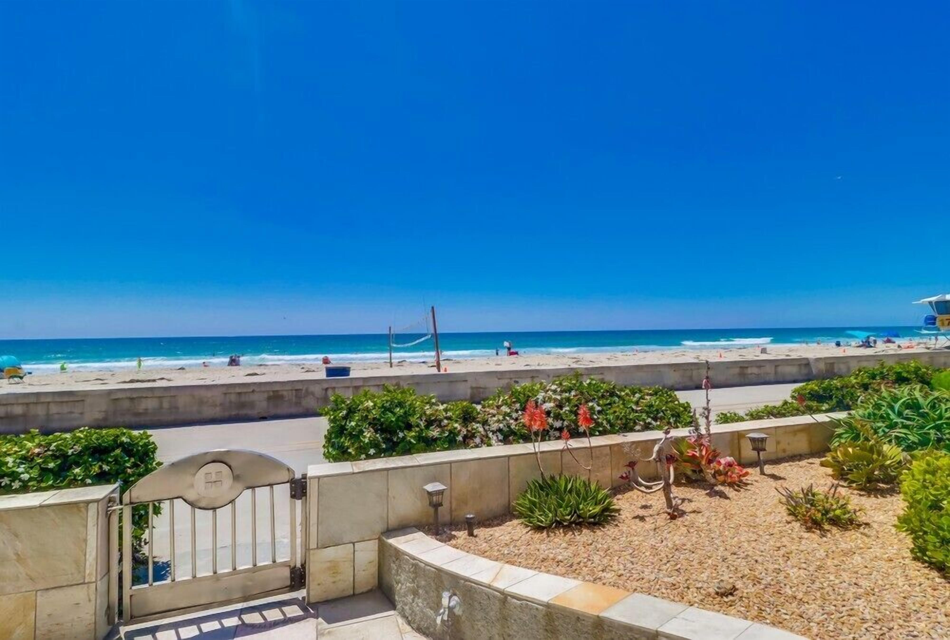 A beachfront property with a gated entrance, a patio area with plants, and a view of the beach and ocean.