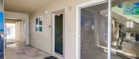 A corridor with a sliding glass door leading to a balcony with a view of a building with a sign that reads "NEW HOTEL."