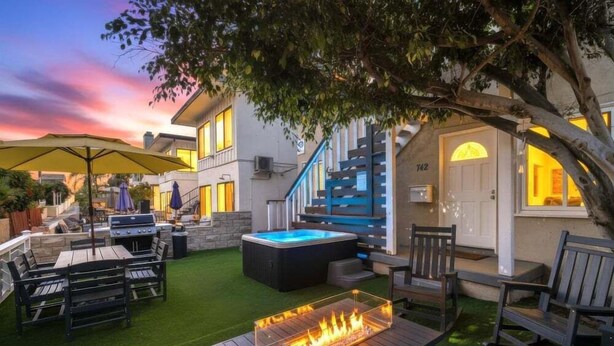Un patio trasero con una parrilla, mobiliario exterior, un jacuzzi y una escalera que lleva a la casa.