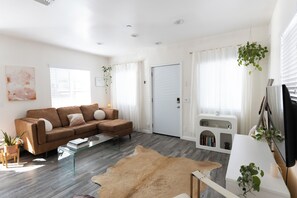 Un salon moderne avec un canapé en cuir marron, une table basse en verre et un meuble de rangement blanc pour l’équipement audiovisuel.