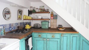 Une cuisine avec des armoires de couleur turquoise, un fourneau et divers ustensiles de cuisine rangés sur des étagères.